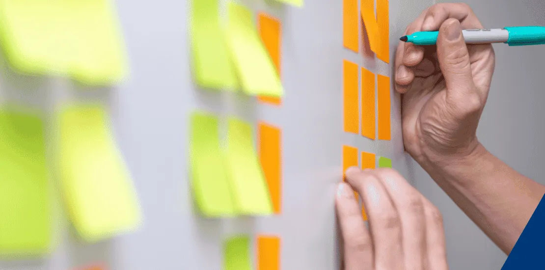 Hand markiert orangefarbene Notizzettel an einer Wand, Scrum-Board?